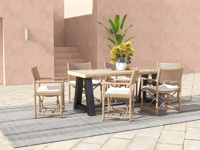 Outdoor dining set with wooden table, woven chairs, yellow flowers, grey rug, and pinkish walls